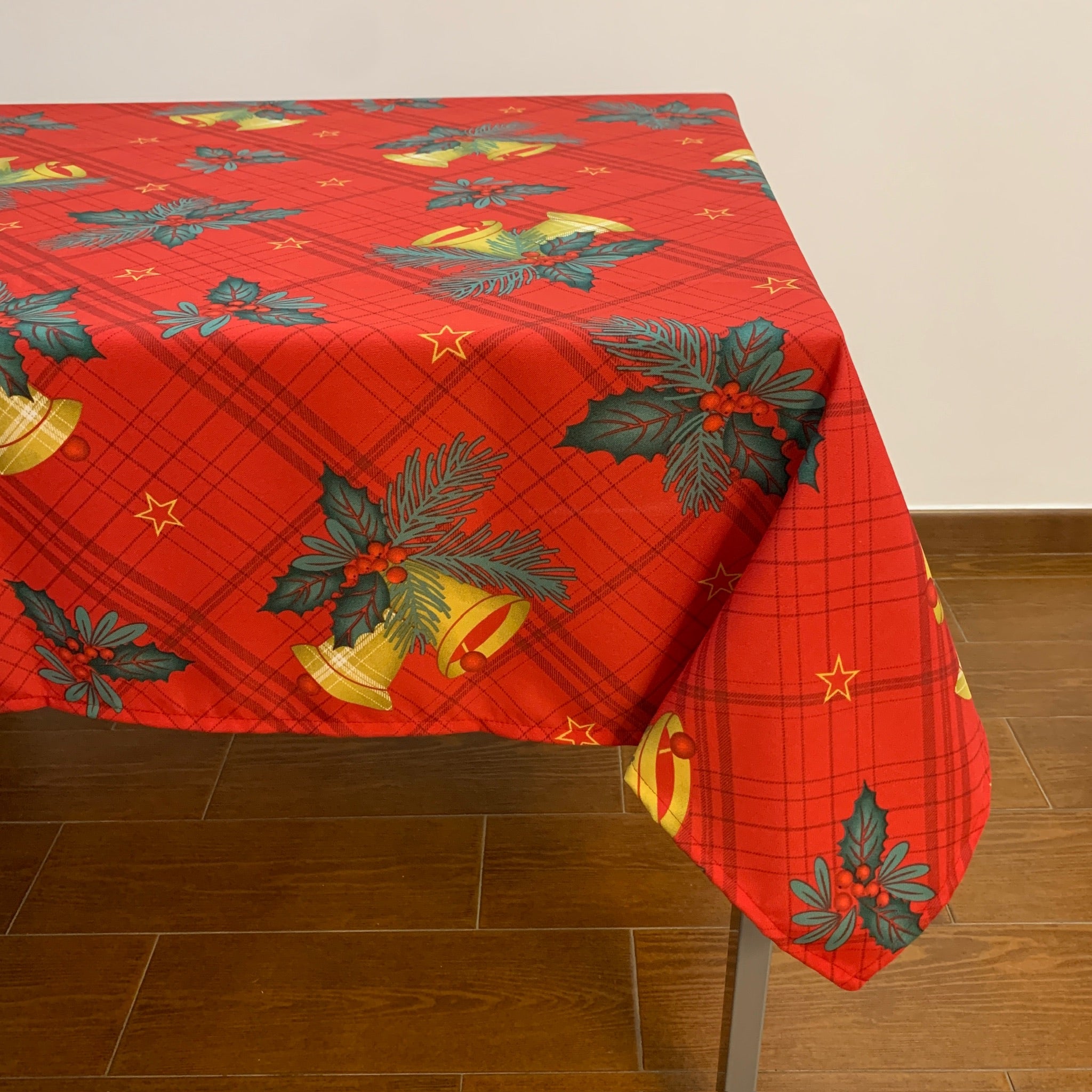 Toalha de mesa de cozinha com fundo vermelho vivo enfeitada com sinos amarrados por azevinho por toda a toalha.