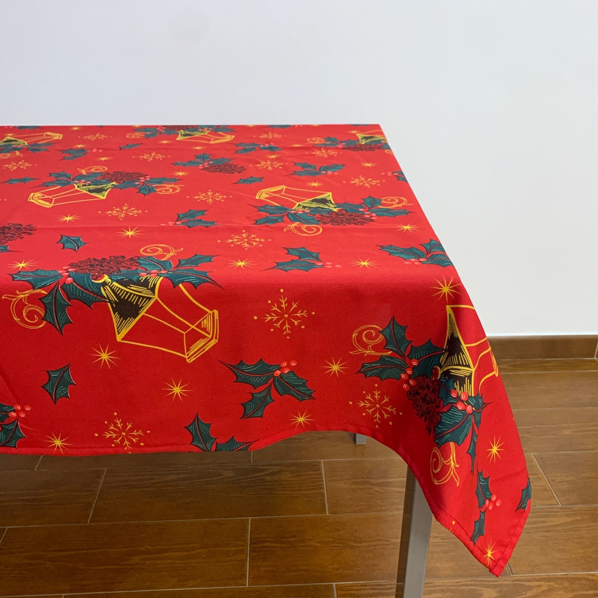 Toalha de Natal vermelha com candeeiros enfeitados com azevinhos espalhados delicadamente por toda a toalha, conjuntamente com pequenas estrelas douradas.